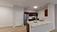 This well-appointed single-floor residence showcases a cohesive modern design carried throughout its living spaces. The kitchen serves as a central highlight, featuring rich dark espresso cabinetry paired with a classic white subway tile backsplash and striking granite countertops. A peninsula island with an undermount sink provides additional workspace and informal gathering space. Stainless steel appliances, including a refrigerator, range, and microwave, complete the functional kitchen layout.

Light hardwood-style flooring flows seamlessly throughout the main living areas and bedrooms, contributing to a bright, unified aesthetic. The bedrooms are well-proportioned, each equipped with ceiling fans and windows fitted with blinds that allow for natural light control. One bedroom features a set of French doors, offering an elegant connection to an adjacent space or exterior area.

Two bathrooms serve the residence, each finished with dark espresso vanity cabinetry, granite-topped counters, and light tile flooring. The primary bathroom includes a large mirror above the vanity and a tiled shower surround, while the secondary bathroom offers a full tub-shower combination. Neutral warm-gray wall tones throughout create a calm, contemporary ambiance that complements the consistent material palette across the entire space.