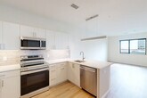 Located in the heart of Wilmington, DE, this well-appointed one-bedroom, one-bathroom residence offers a thoughtfully designed layout across a single floor. Light-toned hardwood flooring flows throughout, complementing the clean white walls and creating a bright, cohesive atmosphere.

The kitchen is a standout feature, showcasing flat-panel white cabinetry that extends to the ceiling for ample storage, a white quartz countertop, and a subway tile backsplash. Stainless steel appliances — including a refrigerator, electric range, built-in microwave, and dishwasher — deliver a modern, functional cooking space. A sleek linear pendant light anchors the kitchen, which opens directly into the living area for an airy, connected feel.

The bedroom is a comfortable, well-proportioned retreat with large windows framing views of the Wilmington skyline, allowing natural light to fill the room. A dedicated closet provides convenient storage.

The bathroom features a glass-enclosed walk-in shower with white tile surround, hardwood-style flooring, and a streamlined vanity. In-unit laundry adds everyday practicality. The entryway, positioned adjacent to the kitchen, offers a clean transition into the living space. This residence combines modern design with efficient use of space in a prime downtown Wilmington location.