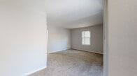 Located at 5818 Newtown Arch in Virginia Beach, Virginia, this single-floor unit offers a straightforward, functional layout designed for comfortable everyday living. The open floor plan, visible in the 3D overview, divides the space into distinct living, sleeping, and kitchen zones while maintaining a cohesive, neutral aesthetic throughout.

The living area is generously sized, featuring wall-to-wall carpet in a warm beige tone and multiple windows dressed with blinds that allow natural light to fill the room. A sliding glass door with vertical blinds provides additional light and outdoor access. The neutral gray and white wall palette keeps the space feeling clean and bright.

The kitchen is equipped with two-tone cabinetry—white upper cabinets and gray lower cabinets—paired with marble-look countertops and a stainless steel sink. A black refrigerator and a range are included, and wood-look vinyl flooring adds a durable, easy-to-maintain surface underfoot.

The bedrooms are carpeted and feature ample closet space, including both standard and walk-in style closets with built-in shelving and hanging rods. The bathroom includes a full tub-shower combination, a toilet, and wood-look vinyl flooring that complements the kitchen's finishes.

Overall, the unit presents a clean, move-in-ready environment with practical storage solutions and consistent finishes throughout.