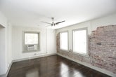 This single-floor space blends industrial character with practical functionality. The main living area is an immediate standout, showcasing rich, dark-stained hardwood floors that run throughout, complemented by a striking exposed brick accent wall that adds texture and warmth to the otherwise neutral, white-painted walls. Multiple windows allow natural light to pour in, while a ceiling fan with an integrated light fixture provides both airflow and ambient lighting. The open layout of the living area offers generous room to arrange furnishings freely.

The kitchen is compact yet well-equipped, featuring dark granite-style countertops, white cabinetry, a double stainless steel sink with a modern faucet, and black appliances including an electric range and an over-the-range microwave. Upper and lower cabinet storage is well-distributed, providing ample organization space.

The bathroom is efficiently designed, incorporating a standalone shower stall with chrome fixtures, a single-sink vanity with under-sink cabinet storage, a mirrored medicine cabinet above, and tile flooring. The layout makes practical use of the available space while keeping a clean, functional aesthetic throughout.