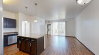 This 2-bedroom, 2-bathroom residence in Denver, CO offers a well-designed, single-floor layout that balances functionality and comfort. The open-concept kitchen and living area serves as the heart of the home, showcasing rich dark cabinetry, granite countertops, a central island with pendant lighting, and a full suite of stainless steel appliances including a refrigerator with ice maker, range, microwave, and dishwasher. Hardwood-style flooring flows throughout the main living area, adding warmth and continuity to the space. A large sliding glass door fills the living room with natural light and provides access to a private balcony with outdoor views. An in-unit stacked washer and dryer is conveniently located off the living area. Both bedrooms feature plush carpeting and ample natural light; the secondary bedroom includes a ceiling fan, while each room offers dedicated closet space. The two bathrooms are finished with stone-look tile flooring, dark vanity cabinetry, white countertops, and one includes a full soaking tub with white tile surround. A connecting hallway ties the layout together, creating a clean and practical flow throughout this Denver residence.
