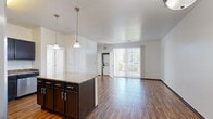 This 2-bedroom, 2-bathroom residence in Denver, CO offers a well-designed, single-floor layout that balances functionality and comfort. The open-concept kitchen and living area serves as the heart of the home, showcasing rich dark cabinetry, granite countertops, a central island with pendant lighting, and a full suite of stainless steel appliances including a refrigerator with ice maker, range, microwave, and dishwasher. Hardwood-style flooring flows throughout the main living area, adding warmth and continuity to the space. A large sliding glass door fills the living room with natural light and provides access to a private balcony with outdoor views. An in-unit stacked washer and dryer is conveniently located off the living area. Both bedrooms feature plush carpeting and ample natural light; the secondary bedroom includes a ceiling fan, while each room offers dedicated closet space. The two bathrooms are finished with stone-look tile flooring, dark vanity cabinetry, white countertops, and one includes a full soaking tub with white tile surround. A connecting hallway ties the layout together, creating a clean and practical flow throughout this Denver residence.