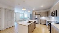 Located on Community Way in Frisco, TX, this single-floor home offers four bedrooms, three bathrooms, and three closets within a thoughtfully designed layout. The open-concept kitchen and living area serves as the heart of the home, featuring light wood-look flooring, a large central island with a white quartz countertop and undermount sink, contemporary wood-grain cabinetry, a tile backsplash, stainless steel appliances, and stylish pendant lighting. The adjacent living room is bright and airy, benefiting from large windows and a ceiling fan, with French doors providing access to an outdoor area. The bedrooms are finished with plush carpeting and ceiling fans, each accompanied by dedicated closet space. Multiple walk-in closets throughout the home are equipped with multi-tiered shelving and hanging rods for ample storage. The three bathrooms are finished in a clean, modern style with light wood-look tile flooring, sleek vanities with white countertops, and illuminated mirrors. One bathroom includes a soaking tub and shower combination. Throughout the home, a neutral, light color palette and consistent finishes create a cohesive and welcoming ambiance.