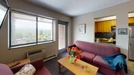 Located at 121 Dryden Rd in Ithaca, NY, this single-floor unit offers a well-organized layout designed to accommodate multiple occupants comfortably. The living area is a welcoming space centered around a sofa and coffee table, with a large window framing lush, tree-lined views of the surrounding Ithaca landscape, allowing generous natural light to fill the room. The adjacent kitchen is efficiently designed, featuring warm oak cabinetry, granite-style countertops with a dark tile backsplash, stainless steel appliances including a refrigerator, dishwasher, microwave, and a gas range, providing everything needed for full meal preparation. A separate dining area accommodates group dining with a table and chairs. The unit includes multiple bedrooms, each carpeted and furnished with a bed, dresser, and desk, making them well-suited for student living. Bedrooms feature windows with adjustable blinds, with some rooms offering elevated views of the Ithaca skyline and surrounding greenery. The bathroom is equipped with a vanity, toilet, and a tub-shower combination with sliding glass doors. The overall ambiance is functional and practical, well-positioned near Cornell University and the amenities of downtown Ithaca.