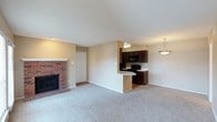 This single-floor residence offers a practical and comfortable open-concept layout that seamlessly connects the living and kitchen areas. The spacious living room is finished with plush wall-to-wall carpeting and anchored by a classic brick fireplace, which serves as a warm and inviting focal point. Neutral-toned walls throughout lend a clean, versatile backdrop suited to a variety of interior styles. A closet adjacent to the fireplace provides convenient storage within the living area. The kitchen is defined by rich, dark wood cabinetry paired with black appliances, including a range and over-the-range microwave. A peninsula counter bridges the kitchen and living space, offering both additional workspace and a casual seating opportunity. A pendant light fixture hangs above the peninsula, adding a touch of character to the area. The kitchen also features hard flooring, contrasting with the carpeted living space and creating a clear, functional distinction between the two zones. The textured ceiling adds a subtle architectural element throughout. Overall, this space offers a cozy yet functional environment with a well-considered layout that balances open living with defined areas for cooking and relaxing.
