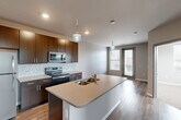 Located at 1330 Big Bend Rd in Twin Oaks, Missouri, this 1-bedroom, 1-bathroom unit offers a thoughtfully designed single-floor layout that maximizes functionality and style. The open-concept kitchen serves as the centerpiece of the living area, showcasing rich dark-wood cabinetry, light quartz countertops, a subway-tile backsplash, and a full suite of stainless steel appliances including a refrigerator, electric range, and microwave. A kitchen island with a double sink and pendant lighting above adds both workspace and visual appeal, flowing seamlessly into the living area, which is brightened by a large window and access to a private entry door. Hardwood-style flooring runs throughout the main living and kitchen areas, lending a warm, cohesive aesthetic. The bedroom offers a comfortable footprint with plush carpeting, a ceiling fan, and multiple windows that invite natural light and outdoor views. A dedicated closet provides convenient storage. The bathroom features a clean, modern design with wood-tone cabinetry, a white vanity countertop, light tile flooring, and a window for natural ventilation. A double-door closet near the kitchen adds additional storage capacity, completing this efficient and contemporary living space.