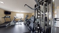 Located at 5001 SW 20th St in Ocala, Florida, this well-equipped fitness center offers a comprehensive workout environment designed to support a wide range of exercise routines. The single-floor facility features durable dark rubber flooring throughout, providing a safe and functional surface for all types of training activities.

The space is outfitted with an extensive selection of cardio equipment, including treadmills, elliptical trainers, stationary bikes, and stair climbers, allowing users to engage in varied cardiovascular workouts. A multi-station strength training machine serves as a centerpiece for resistance-based exercise, complemented by a vertical knee raise and pull-up tower for bodyweight training. Stability balls and additional accessories are also available for functional fitness routines.

Large mirrors line one wall, visually expanding the space while allowing users to monitor their form during exercise. Multiple windows with blinds admit natural light, creating a bright and welcoming atmosphere. Recessed lighting provides consistent illumination throughout. A wall-mounted television offers entertainment during cardio sessions, and a wall clock keeps users on schedule.

The warm, neutral-toned walls and textured ceiling contribute to a clean, no-frills aesthetic focused on functionality. The facility is accessible via a dedicated entry door with an emergency exit, ensuring convenience and safety for all users.