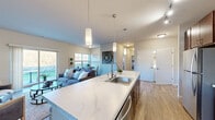 Located at 2212 New Port Vista Drive in Grafton, Wisconsin, this well-designed 2-bedroom, 2-bathroom single-floor residence offers a thoughtful open-concept layout filled with natural light and modern finishes. The combined kitchen and living room serves as the heart of the home, featuring a large island with a striking marble-look countertop, an undermount sink, pendant lighting, rich dark wood cabinetry, and stainless steel appliances. A breakfast bar with seating adds casual dining convenience. The living room is anchored by a tile-surround fireplace and opens directly to an outdoor patio through sliding glass doors, bringing in abundant natural light and outdoor views. Light wood-style flooring flows throughout the main living areas, complementing the neutral color palette. The primary bedroom is a generously sized retreat with plush carpet, a ceiling fan, and bright windows overlooking greenery. It connects to a walk-in closet with built-in shelving and a full bathroom featuring dark wood vanity cabinetry and a large mirror. The second bedroom is comfortable and well-lit, with easy hallway access to the second full bathroom. A dedicated closet and in-unit laundry access provide practical storage solutions throughout.