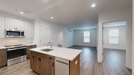 Located at 373 E Main St in Branford, Connecticut, this single-floor unit showcases a clean, contemporary design with high-quality finishes throughout. The open-concept layout connects the kitchen and living area seamlessly, creating a bright and functional living space. Recessed lighting and natural light from multiple windows contribute to an airy, welcoming atmosphere, complemented by durable wood-tone flooring that runs consistently throughout the main areas.

The kitchen serves as a central focal point, featuring a large island with a white quartz countertop, an undermount sink, and warm wood-toned lower cabinetry paired with crisp white upper cabinets. Stainless steel appliances, including a refrigerator, range, microwave, and dishwasher, complete the space. The living area is generously sized with a wall-mounted mini-split HVAC unit providing efficient climate control.

The bedrooms offer comfortable proportions with ample closet space and additional mini-split units. The bathrooms are finished with large-format light marble-style tile flooring, warm wood vanities topped with white countertops, and sleek fixtures. One bathroom includes a glass-enclosed tub and shower combination. The overall aesthetic is modern, clean, and move-in ready.