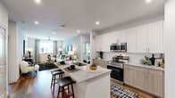 Located at 255 Williamsburg Pkwy in Fate, Texas, this thoughtfully designed single-story residence offers a seamless open-concept layout that connects the kitchen, dining, and living areas into one cohesive, welcoming space. The kitchen is a standout feature, boasting granite countertops, a large center island with bar seating, white upper cabinetry, warm-toned lower cabinetry, a subway tile backsplash, and stainless steel appliances including a range and over-the-range microwave. Wood-look flooring runs throughout, adding warmth and continuity to every room. The living area is bright and inviting, with natural light streaming through large windows dressed in patterned drapes, complemented by a ceiling fan overhead. Two well-appointed bedrooms each feature soft accent walls in calming teal and sage tones. The primary bathroom offers a granite-topped vanity with light wood cabinetry, a tiled shower, and direct access to a spacious walk-in closet with built-in shelving and hanging rods. The second bathroom mirrors the same refined aesthetic with a granite vanity and tiled shower. Clean white walls, recessed lighting, and consistent flooring throughout create a polished, modern ambiance across the entire residence.