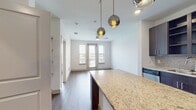 This contemporary 600 square foot apartment offers a thoughtfully designed one-bedroom layout. The heart of the home is an open-concept kitchen and living area, showcasing a gourmet kitchen with dark wood cabinetry, stainless steel appliances, and a spacious island with granite countertops. Pendant lighting adds a touch of elegance, while the mosaic tile backsplash provides visual interest.

The bedroom, measuring 140 square feet, features large windows that flood the space with natural light and offer exterior views. A ceiling fan ensures comfort, and the room connects to a well-appointed bathroom with a granite-topped vanity and large mirror.

Throughout the apartment, durable wood-look flooring creates a cohesive and modern aesthetic. The unit boasts practical amenities, including an in-unit laundry room with full-sized washer and dryer, and a walk-in closet for ample storage.

A standout feature is the balcony access, providing an outdoor extension of the living space. The apartment's design maximizes functionality in its compact footprint, with clean lines and a neutral color palette that allows for personalization. Recessed lighting and strategically placed windows contribute to the bright and airy ambiance of this contemporary urban dwelling.