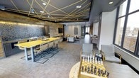 This single-floor amenity lounge is designed with a contemporary aesthetic that blends industrial and modern elements throughout. The space is immediately defined by its striking ceiling installation — a web of gold linear strands that crisscross against a dark backdrop, creating a dramatic and artistic focal point overhead. Large-format tile flooring in a neutral gray tone grounds the space and flows consistently throughout.

A generously sized bar-height communal table in yellow-toned wood, paired with industrial-style metal chairs, anchors the left side of the room and is positioned near a built-in wet bar or kitchenette area, making it well-suited for social gatherings. A wall-mounted flat-screen TV and a textured stone accent wall add character to this zone.

Moving deeper into the lounge, a comfortable seating area with upholstered chairs and a coffee table provides a quieter, lounge-style retreat. The corridor beyond leads to additional seating nooks, offering a sense of depth and varied spaces within the layout.

In the foreground, a dedicated game area features an oversized chess set on a yellow-and-gray board table, reinforcing the space's playful yet sophisticated character. The overall ambiance is modern, energetic, and thoughtfully curated.