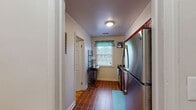 This single-story home offers a well-organized layout with a variety of distinct living spaces. The galley-style kitchen is efficiently designed, featuring rich cherry wood cabinetry, granite countertops, stainless steel appliances including a gas range and full-size refrigerator, and durable tile flooring. A window adorned with a teal valance brings in natural light, while a nearby door provides convenient access to an adjacent room or exterior. The living area is warm and inviting, with gleaming hardwood floors, multiple windows dressed in teal curtains that allow ample natural light, and enough space to accommodate both a seating area and a small dining arrangement with a glass-top table. Three bedrooms offer varied character: the primary bedroom features plush carpeting, dual windows for cross-ventilation, and generous floor space; a second bedroom offers a cozy, intimate feel with a classic iron bed frame; and a third bedroom provides a quiet retreat with soft carpeting and decorative accents. The full bathroom is finished with classic black-and-white tile detailing, a granite-topped vanity with cherry wood cabinetry, and a tub-shower combination, maintaining a clean, timeless aesthetic throughout.