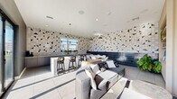 Located at 1100 West Temple Street in Los Angeles, this thoughtfully designed amenity lounge offers a cohesive blend of modern aesthetics and functional comfort across a single floor. The space is immediately distinguished by its bold geometric tile work — a striking black-and-white triangular mosaic pattern that wraps across the walls, creating a dynamic visual backdrop throughout.

The kitchen area serves as a central focal point, featuring sleek gray cabinetry, a substantial granite-topped island with bar seating, and pendant lighting that adds warmth and depth. Full-length windows alongside the kitchen draw in generous natural light while framing views of the surrounding Los Angeles cityscape.

Adjacent to the kitchen, a dining area provides an intimate setting for gathering, complemented by the deep navy tile accent wall that adds a sophisticated contrast to the lighter tones elsewhere. The lounge area is furnished with plush gray sofas and stylish accent chairs with distinctive yellow-accented frames, arranged around a media console and wall-mounted display.

A slatted wood partition wall adds architectural texture, subtly dividing the lounge zones while maintaining an open, airy feel. Large-format light tile flooring runs seamlessly throughout, unifying the space. Sliding glass doors open directly onto an outdoor terrace, extending the usable area and offering additional seating with open-air city views — a standout feature of this vibrant urban retreat.