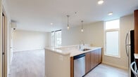 This contemporary two-bedroom, two-bathroom residence spans two floors, offering a well-designed layout with thoughtful finishes throughout. The main floor features an open-concept kitchen and living area bathed in natural light from large windows. The kitchen is a standout, showcasing a generous peninsula with white quartz countertops, warm wood cabinetry, stainless steel appliances including a refrigerator, range, microwave, and dishwasher, and elegant pendant lighting overhead. Light wood-style flooring runs throughout the main level, enhancing the bright, modern ambiance.

The upper floor houses both bedrooms, each offering a comfortable and private retreat. The spacious primary bedroom includes a wall-mounted climate control unit and access to a closet, while the second bedroom features large windows with outdoor views and plush carpeting. Both bedrooms are served by two full bathrooms, each finished with wood-toned vanities, white countertops, and a shower-tub combination. Additional conveniences include two closets with wire shelving systems, a dedicated laundry area, and in-unit staircase access between floors. The overall aesthetic is clean, modern, and move-in ready.