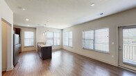 This single-floor residence on NW Valley View Road in Independence, Missouri, presents a thoughtfully designed open-concept layout finished with contemporary details throughout. The living and dining area is expansive and bright, featuring wood-look plank flooring and multiple large windows dressed with horizontal blinds that allow generous natural light to fill the space. Neutral-toned walls and recessed lighting contribute to the clean, modern aesthetic.

The kitchen is a standout feature, centered around a substantial island with a light quartz countertop, double stainless steel sink, and stylish pendant lighting overhead. Dark espresso-toned cabinetry extends along the wall, complemented by a tile backsplash and stainless steel appliances including an electric range and microwave. The layout creates a seamless connection between the kitchen and living areas, ideal for entertaining.

The bedrooms are carpeted for comfort, each offering natural light through blinds-fitted windows. One bedroom includes a ceiling fan. The primary bathroom features a dual-sink vanity with dark cabinetry, a large mirror, and a glass-enclosed shower. A secondary bathroom provides a single-sink vanity and a shower-tub combination, finished with matching wood-look flooring consistent with the rest of the unit.