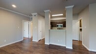 This single-floor residence offers a thoughtfully designed open-concept layout that seamlessly connects the living, dining, and kitchen areas. Rich, dark hardwood flooring flows throughout the main living spaces, complemented by neutral gray walls, white trim, and crown molding that lend a clean, polished aesthetic.

The living room is spacious and airy, featuring a ceiling fan, large windows that invite abundant natural light, and a glass-panel door providing direct outdoor access. Decorative columns elegantly frame the transition between the living area and the kitchen, adding an architectural character to the open floor plan.

The kitchen is a standout feature, offering dark espresso cabinetry, light granite countertops, a tile backsplash, and a full suite of stainless steel appliances including a refrigerator, electric range, microwave, and dishwasher. A peninsula-style breakfast bar provides a convenient spot for casual dining and meal prep.

A dedicated in-unit laundry area houses a full-size side-by-side washer and dryer, adding everyday convenience. The bathroom features a soaking tub with a tiled surround and a combination showerhead, creating a relaxing retreat. Multiple interior doors throughout suggest well-defined bedroom and closet spaces, rounding out this functional and attractive residence.