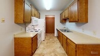 This well-appointed one-bedroom, one-bathroom unit in Sioux Falls, South Dakota, offers a practical and comfortable single-floor layout. The galley-style kitchen is lined with warm oak cabinetry on both sides, providing generous storage above and below the countertops. White appliances, including a range, microwave, refrigerator, and dishwasher, are all included, while light tile flooring and a textured ceiling complete the space. A ceiling fan overhead adds to the functionality of the adjacent dining area, which opens naturally toward the kitchen. The living room is bright and open, featuring soft wall-to-wall carpeting, a sliding glass door that invites natural light and outdoor views of mature trees, and a wall-mounted heating unit. The bedroom is a comfortable size, carpeted throughout, and includes a ceiling fan with light fixture, a window with blinds for natural light and privacy, and a baseboard heater. A closet with sliding doors provides ample storage. The bathroom features a full tub-shower combination, a toilet, a vanity with countertop, and a wall-mounted oak cabinet for additional storage. Tile flooring ties the room together neatly. Throughout the unit, warm wood trim accents and neutral wall tones create a cohesive, move-in-ready atmosphere.