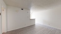 This single-floor unit offers a practical and efficiently designed layout across a compact footprint. The open-concept living and kitchen area serves as the heart of the space, featuring light gray wood-look flooring, white walls, and a textured popcorn ceiling. A ceiling fan provides air circulation, while a half-wall peninsula visually separates the kitchen from the living area. The kitchen is equipped with white cabinetry, ample upper and lower storage, a built-in electric range, and a single-basin sink beneath a window that allows natural light in.

The bedroom is carpeted and includes a sliding closet and a window offering an outdoor view. An adjoining dressing area features built-in cabinetry with a vanity counter and mirror, adding useful storage. Two bathrooms serve the unit; one includes a full tub-shower combination with classic tile surround in neutral pink tones and a window for natural light.

Throughout, the unit maintains a clean, neutral palette with consistent flooring choices and white trim, creating a cohesive and functional living environment well-suited for efficient everyday use.