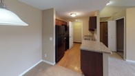 Located at 20969 Woodland Glen Dr in Northville, Michigan, this single-floor residence offers a well-organized layout with a cohesive, neutral color palette of warm beige tones and white trim throughout. The spacious living room serves as the heart of the home, featuring plush carpeting, a ceiling fan with light fixture, built-in shelving, and a large window with vertical blinds that invites natural light and outdoor views. A pendant light marks the transition into the open dining area, which flows seamlessly into the kitchen. The kitchen is equipped with dark wood cabinetry, black appliances including a refrigerator and range, a granite-style countertop with an undermount sink, and a peninsula that connects to the living space. Hardwood-style flooring in the kitchen adds a practical, easy-care surface. Two well-sized bedrooms are finished with soft carpeting, neutral walls, and windows providing natural light. The full bathroom features a single vanity with a tile-surround countertop, dark wood cabinetry, a soaking tub with shower, and a lighted mirror. A second half bathroom offers a matching vanity with tile countertop and additional storage. The overall ambiance is clean, comfortable, and move-in ready.