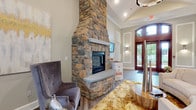 Located at 6450 Mercantile Dr E in Frederick, Maryland, this single-floor community clubhouse offers a sophisticated and welcoming environment defined by high-end finishes and thoughtful design. The main lounge area is anchored by a dramatic floor-to-ceiling stacked stone fireplace, which serves as the architectural centerpiece of the space. Soaring vaulted ceilings with elegant wainscoting panels, a modern ring chandelier, and recessed lighting create an airy, upscale atmosphere. Herringbone-patterned luxury vinyl plank flooring flows seamlessly throughout, tying each area together cohesively. The lounge is furnished with tufted seating and accented by curated artwork, offering a refined yet comfortable gathering space. Adjacent to the lounge, a fully equipped kitchen features warm wood cabinetry, granite countertops, an undermount sink, and built-in appliances, making it ideal for resident events and gatherings. Large windows flood the kitchen and dining area with abundant natural light and offer serene views of the surrounding greenery. The dining nook accommodates multiple seating arrangements around round café-style tables, complemented by intricate carved wood wall art and a whitewashed sideboard that add an artisanal touch. Overall, the space blends transitional and contemporary design elements to create an inviting, functional, and visually striking community hub.