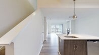 This two-story residence offers 1,950 square feet of living space across two floors, with 760 sq ft on the ground level and 1,190 sq ft on the upper level. The open-concept main floor features a combined kitchen and living room with light hardwood flooring and soaring high ceilings that enhance the sense of space. The living room is anchored by a tile-surround fireplace and floor-to-ceiling sliding glass doors that open onto a private balcony, offering views of the surrounding community. The modern kitchen is well-appointed with white upper cabinetry, dark lower cabinetry, stainless steel appliances including a gas range, microwave, and refrigerator, and a quartz-topped island with an undermount sink and pendant lighting. The upper floor hosts three bedrooms, including a generous primary suite spanning 850 sq ft, all featuring plush carpet flooring and ceiling fans. One bedroom includes direct balcony access via sliding glass doors. The single full bathroom includes a tiled tub-shower combo, a dark wood vanity with a single sink, and hardwood-style flooring. Additional highlights include a carpeted walk-in closet with wire shelving, a hallway, and an overall clean, neutral aesthetic throughout.