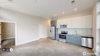 Located at 614 Rigsbee Ave in Durham, NC, this contemporary 2-bedroom, 2-bathroom residence offers a thoughtfully designed single-floor layout with clean modern finishes throughout. The open-concept kitchen and living area serves as the heart of the home, featuring polished concrete floors, floor-to-ceiling windows that flood the space with natural light, and views of the surrounding neighborhood. The kitchen is equipped with stainless steel appliances — including a French door refrigerator, electric range, and built-in microwave — complemented by two-tone cabinetry in white and muted blue-grey, granite countertops, and a white subway tile backsplash. Both bedrooms are generously proportioned, highlighted by elevated ceilings, ceiling fans, and concrete flooring. The primary bedroom includes access to a well-appointed walk-in closet with wire shelving systems. The two bathrooms mirror each other in style, each featuring granite-topped vanities with dark hardware, large framed mirrors, and white tile surrounds — one with a soaking tub and one with a walk-in shower. A dedicated laundry area and ample closet storage throughout add to the unit's practicality. The bright, clean hallway with recessed lighting connects all rooms seamlessly, completing this well-organized modern residence.