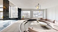 This opulent lobby space, spanning 195 square meters, showcases a harmonious blend of modern luxury and classic elegance. The grand entrance is marked by floor-to-ceiling glass doors, welcoming visitors into a space dominated by exquisite marble features. Dark marble columns and accents contrast beautifully with light marble walls, creating a striking visual impact.

The lobby's centerpiece is a stunning marble water feature, adding a touch of serenity to the bustling space. A mezzanine level, adorned with ornate gold railings, overlooks the main floor, enhancing the sense of grandeur. The ceiling is adorned with crystal chandeliers, casting a warm glow throughout.

Seating areas are thoughtfully arranged, featuring curved sofas and modern coffee tables that invite relaxation. Large windows flood the space with natural light, offering views of the surrounding area. The floor combines polished marble inlays with plush carpeting, seamlessly blending luxury with comfort.

Attention to detail is evident in the carefully chosen lighting fixtures, from pendant lights to recessed ceiling lights, creating a warm and inviting atmosphere. This lobby not only serves as a functional entrance but also as a statement of sophistication and style, setting the tone for the entire building.