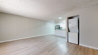 This well-appointed single-floor unit offers a clean, modern aesthetic highlighted by light hardwood-style flooring and a neutral color palette that flows seamlessly throughout the space. The open living area is generously sized, featuring a large window with vertical blinds that allows abundant natural light to fill the room, complemented by a textured ceiling and crisp white baseboards.

The kitchen is a standout feature, outfitted with white shaker-style cabinetry, granite-look countertops, and a full suite of stainless steel appliances including a refrigerator, electric range with overhead ventilation hood, and dishwasher. A peninsula counter provides additional prep space and creates a natural transition between the kitchen and living areas. A window above the sink brings in additional daylight.

Conveniently tucked adjacent to the living area is a dedicated in-unit laundry alcove housing a stacked washer and dryer, adding a practical and desirable convenience.

Two bathrooms serve the unit, each finished consistently with white cabinetry and granite-look countertops. One bathroom features a shower stall with sliding glass doors, while the second offers a full tub-shower combination. Both maintain the same light, airy finishes seen throughout the rest of the unit, creating a cohesive and polished overall ambiance.