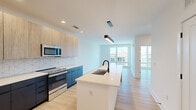 This thoughtfully designed one-bedroom, one-bathroom unit offers a contemporary living experience across a single floor. Light wood-tone flooring flows consistently throughout, lending warmth and cohesion to the open layout.

The kitchen is a standout feature, showcasing a two-toned cabinetry design with light wood upper cabinets and deep navy-blue lower cabinets paired with crisp white quartz countertops. A geometric tile backsplash adds visual interest, while a full suite of stainless steel appliances — including a side-by-side refrigerator, electric range, built-in microwave, and dishwasher — ensures modern functionality. A central island with an undermount sink and matte black faucet serves as both a prep area and a visual anchor for the open-concept living space.

The living area is bright and open, benefiting from large windows that invite generous natural light and offer views of the surrounding neighborhood. The bedroom is a comfortable, well-proportioned retreat with oversized windows, a ceiling fan, and ample wall space.

The bathroom features a long, navy-blue floating vanity with a white countertop, a large mirror with linear lighting, matte black hardware, and a tiled walk-in shower. A dedicated laundry area with a stacked washer and dryer provides added convenience within the unit.
