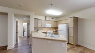 This single-story, 3-bedroom, 2-bathroom home offers a functional and comfortable layout across a generously sized floor plan. The open-concept living and dining area is anchored by warm hardwood-style flooring and a ceiling fan with integrated lighting, creating a bright and welcoming atmosphere. A pendant light marks the transition toward the entryway, where natural light filters in through the front door.

The kitchen is well-equipped and efficiently designed, featuring a wraparound peninsula with a built-in sink, light-toned cabinetry extending to the ceiling, a smooth-top range, built-in microwave, and a full-size refrigerator. A skylight-style flush fixture provides ample overhead illumination, and the hardwood-style flooring continues throughout.

The three bedrooms offer a comfortable retreat; two feature plush carpeting and ceiling fans, with large windows that invite natural light and outdoor views. The primary bedroom includes access to a dedicated closet area. The additional bedrooms also benefit from multiple windows, enhancing the sense of airiness.

Both bathrooms are finished with wood-look flooring, vanities with under-sink storage, and tub-shower combinations. Clean, neutral tones throughout maintain a cohesive and understated aesthetic. The attached single-car garage provides convenient parking and additional storage space, completing this practical and well-organized home.