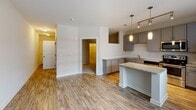 This single-floor unit offers a thoughtfully designed open-concept layout that seamlessly connects the main living areas. The kitchen serves as a central highlight, outfitted with grey shaker-style cabinetry, granite countertops, and a classic white subway tile backsplash. A full suite of stainless steel appliances—including an electric range, over-the-range microwave, dishwasher, and refrigerator—provides a polished, functional workspace. A peninsula with pendant lighting adds both additional prep space and a natural division between the kitchen and the expansive living area.

Wood-style flooring flows throughout the main living space, hallway, and bedroom, lending warmth and continuity to the interior. The living area is generously proportioned, with neutral-toned walls and a wide window that invites natural light. The hallway features two panel-style doors with brushed nickel hardware, providing access to storage and additional rooms.

The bathroom is cleanly finished with light tile flooring, a granite-topped vanity with an undermount sink, and brushed nickel fixtures. The overall design aesthetic is contemporary and cohesive, with a neutral palette and modern finishes maintained consistently throughout the space.