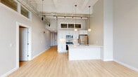 Located at 628 Ellicott St in Buffalo, NY, this 2-bedroom, 2-bathroom loft-style residence blends industrial character with contemporary design. The open-plan living, dining, and kitchen area is the heart of the home, showcasing soaring ceilings with exposed ductwork, track lighting, and oversized industrial-framed windows that flood the space with natural light and offer views of the surrounding neighborhood. Light hardwood flooring runs throughout, complementing the bright, neutral palette. The modern kitchen features white cabinetry, a hexagonal tile backsplash, stainless steel appliances, and a peninsula with a sink — ideal for both cooking and casual dining. The primary bedroom impresses with dramatically tall ceilings, transom windows, and direct access to a well-appointed bathroom. The second bedroom features an exposed brick accent wall and dual closets, adding warmth and texture to the space. Three closets and an in-unit laundry room provide excellent storage and convenience. Both bathrooms are finished with marble-look tile, white vanities, gold-toned fixtures, and a glass-enclosed walk-in shower, delivering a polished, upscale aesthetic. The hallway connects all areas with a clean, modern flow, completing this thoughtfully designed urban residence.