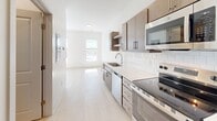 Located at 106 S Buchanan St in Spring Lake, Michigan, this efficiently designed unit offers a clean, modern aesthetic throughout its single-floor layout. Light-toned luxury vinyl plank flooring runs continuously throughout the space, enhancing the bright and airy atmosphere created by large windows that invite abundant natural light and provide views of the surrounding area.

The kitchen is a standout feature, appointed with stainless steel appliances including an electric range, over-the-range microwave, refrigerator, and dishwasher. Light or dark wood cabinetry — depending on the unit configuration — pairs with crisp white quartz countertops and a classic white subway tile backsplash, delivering a polished, contemporary look. The kitchen flows directly into the open living area, creating a seamless and functional living space.

The main living area is generously proportioned relative to the unit's overall footprint, with tall ceilings and clean white walls that amplify the sense of openness. Two louvered doors provide access to closet storage, while an additional door leads to a utility area housing stacked in-unit laundry. Recessed lighting and an electrical panel are neatly integrated. The overall ambiance is fresh, minimal, and move-in ready, making this Spring Lake unit an efficient and stylish place to call home.