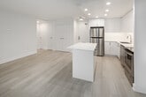 Located at 30 Edith Drive in Toronto's midtown neighbourhood, this unit presents a clean, modern aesthetic defined by a bright, open-concept layout and light hardwood-style flooring that runs consistently throughout the space. Large floor-to-ceiling windows along the living and sleeping areas flood the interior with natural light while framing lush, tree-lined views, contributing to a calm and airy atmosphere. Baseboard heating units run beneath the windows, ensuring comfortable living year-round.

The kitchen is a standout feature, outfitted with high-gloss white cabinetry extending to the ceiling, a white quartz countertop with a waterfall-edge island, and a full suite of stainless steel appliances including a refrigerator, electric range, built-in dishwasher, and over-the-range microwave. The crisp white palette and recessed lighting give the kitchen a polished, contemporary feel.

The bedrooms are well-proportioned, bright spaces with large windows and roller blinds. A dedicated in-unit laundry area with a stacked washer and dryer adds everyday convenience. The bathroom is finished in an all-white scheme, featuring a soaker tub with overhead shower, a clean vanity with under-mount sink, and tile flooring, completing the unit's cohesive modern design.
