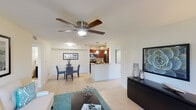 This single-floor residence offers a thoughtfully designed open-concept layout that seamlessly connects the living, dining, and kitchen areas. Light-tone ceramic tile flooring flows throughout the main spaces, complemented by ceiling fans that enhance airflow and comfort. The living room is bright and inviting, featuring a sliding glass door that opens to a private patio, allowing natural light to fill the space. The kitchen is well-equipped with rich cherry wood cabinetry, granite countertops, stainless steel appliances, a built-in microwave, and track lighting overhead. A breakfast bar connects the kitchen to the dining area, which comfortably accommodates a full dining set. The primary bedroom is generously sized, featuring a ceiling fan, large windows with outdoor views, and access to a walk-in closet with built-in shelving. The second bedroom is equally comfortable with its own ceiling fan and ample natural light. Two full bathrooms serve the residence, each featuring tiled shower-tub combinations and tile flooring. A dedicated laundry room with washer and dryer hookups, built-in shelving, and an electrical panel provides added practicality. Overall, the space presents a clean, functional, and comfortable living environment.