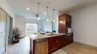Located at 653 Amherst Rd in Sunderland, Massachusetts, this single-floor residence offers a thoughtfully designed layout with modern finishes throughout. The open-concept kitchen is a standout feature, showcasing rich dark wood cabinetry, granite countertops, a center island with a stainless steel sink, pendant lighting, and stainless steel appliances including a dishwasher and refrigerator. A vibrant teal tile backsplash adds a pop of color to one kitchen area, complementing the clean white upper cabinetry. Light wood-style flooring flows through the main living areas, enhancing the bright and airy ambiance. The living room is generously proportioned, featuring a ceiling fan, large sliding glass doors that open to a private balcony with outdoor views, and ample natural light. The bedrooms are carpeted for comfort, each with ceiling fans or light fixtures, windows with blinds, and well-sized footprints. The bathrooms are designed with accessibility in mind, featuring safety grab bars, wood-style flooring, granite-topped vanities with rich wood cabinetry, and spacious layouts with roll-in shower areas. Throughout the space, neutral tones and clean architectural lines create a contemporary and welcoming atmosphere.