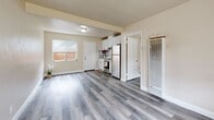 Located at 1555 164th Ave in San Leandro, California, this efficiently designed 2-bedroom unit makes excellent use of its single-floor layout. The open living area connects seamlessly to the kitchen, which is equipped with white cabinetry, a mosaic tile backsplash, a gas range, and a full-size refrigerator. A window at the front of the living space lets in natural light and provides a view of the outdoor surroundings. Consistent grey-toned luxury vinyl plank flooring runs throughout the entire unit, lending a clean, cohesive aesthetic to every room. The two bedrooms are simply appointed with neutral beige walls and windows that allow for natural light — one bedroom features a view of the neighboring exterior. A narrow hallway lined on both sides with sliding-door closets leads to the bathroom, which features a white vanity with a tile backsplash and a mirrored medicine cabinet above. The overall palette of warm neutrals and crisp white trim creates a bright, functional atmosphere. The unit is thoughtfully laid out to maximize utility within its compact footprint, making it a practical and move-in-ready space.