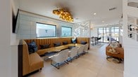 Located in Fort Worth, TX, this single-floor amenity lounge at Dakota Street is designed to impress with a sophisticated blend of modern finishes and inviting social spaces. The open-plan layout flows seamlessly between distinct zones, including a media lounge, communal kitchen, dining areas, and a relaxed seating lounge.

The media lounge features a dramatic textured wall clad in large-format tile panels, a wall-mounted flat-screen TV, and an elegant multi-bulb chandelier that adds warm ambient light. Cognac leather seating and a low-profile wood coffee table complete the intimate atmosphere.

The kitchen and bar area is outfitted with rich wood cabinetry, a stainless steel French door refrigerator, quartz countertops, a tile backsplash, and built-in appliances, providing a fully functional space for entertaining. Open shelving with decorative accents adds a refined touch.

A generous lounge area showcases a long, channel-tufted caramel velvet banquette backed by windows that frame sweeping views of the Fort Worth skyline and surrounding green spaces. A sculptural gold chandelier overhead and a mix of modern seating complete this social hub.

The sun-drenched dining area is surrounded by floor-to-ceiling sliding glass doors and tray ceilings with integrated lighting, inviting abundant natural light and direct access to an outdoor terrace with unobstructed city and park views.