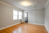 This single-floor unit offers a well-organized layout with classic architectural details throughout. The main living area is bright and welcoming, featuring warm hardwood floors, soft gray walls, and elegant crown molding that adds a refined touch to the space. A double-pane window allows natural light to filter in, offering views of the surrounding cityscape, while a traditional cast-iron radiator provides efficient heating. The textured ceiling adds subtle character to the room.

The bedroom continues the same hardwood flooring and crown molding found throughout the unit. It includes a dedicated closet alcove, a large window with blinds for privacy, and ample wall space, creating a comfortable and functional retreat.

The kitchen is equipped with stainless steel appliances, including a full-size refrigerator and an electric range, complemented by white cabinetry, laminate countertops, and a sink. Dark slate-style tile flooring grounds the space and contrasts cleanly with the lighter cabinetry. A small window provides ventilation.

The bathroom is efficiently designed, featuring the same slate-style tile flooring as the kitchen, a toilet, pedestal sink, and a medicine cabinet, keeping the space clean and practical.

Overall, the unit blends classic pre-war details with functional modern amenities, creating a cohesive and livable space.