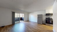 Located at 5474 Reservoir Dr in the College Area neighborhood of San Diego, CA, this single-floor unit offers a clean, functional layout with consistent wood-look flooring flowing throughout every room. The open living area is a standout feature, bathed in natural light from a large sliding glass door that opens onto a private balcony with views of surrounding greenery. A textured ceiling adds subtle character to the bright, white-walled interior. The kitchen is well-appointed with white shaker-style cabinetry, dark countertops, and stainless steel appliances including a refrigerator, range, and microwave. The layout efficiently connects the kitchen to the main living space, creating an open and practical flow. A dedicated bedroom area offers ample space with access to a hallway that leads to the bathroom and closet. The bathroom features a white vanity with dark countertops, a wide mirror with overhead lighting, and a glass-enclosed shower, presenting a modern and refreshed aesthetic. Ceiling vents ensure climate comfort throughout. The unit's overall design is clean, minimal, and move-in ready, suited for those seeking a comfortable residence in San Diego.