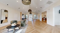Located at 708 Glamorgan Way in Rock Hill, SC, this thoughtfully designed single-floor space blends modern aesthetics with functional versatility. The interior is anchored by striking herringbone-patterned hardwood flooring that flows seamlessly throughout, complementing the bright, neutral color palette of warm white walls and crisp trim.

The main gathering area is expansive and airy, featuring soaring vaulted ceilings adorned with stylish woven pendant light fixtures that add warmth and texture. A signature arched transom window above double French doors floods the space with natural light while serving as a dramatic architectural focal point. Flanking windows further enhance the brightness and openness of the room.

A well-appointed kitchenette offers dark cabinetry, open wood shelving, glossy subway tile backsplash, a built-in beverage cooler, microwave, and sink — ideal for hosting or everyday convenience. Adjacent to the kitchenette is a cozy dining nook with booth-style seating beneath pendant lighting, creating an intimate setting within the larger open floor plan.

A dedicated workstation area with built-in shelving and desk space provides a functional workspace, while a lounge zone with plush seating and a wall-mounted television rounds out the amenities. Clean crown molding, recessed lighting, and carefully curated décor details throughout contribute to the polished, welcoming ambiance of this versatile space.