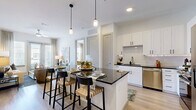Located in Frisco, TX, this thoughtfully designed single-floor residence offers two bedrooms and two bathrooms within a comfortable and efficiently laid-out floor plan. The living room is bright and welcoming, featuring light hardwood-style flooring, soft sage-toned accent walls, and large glass doors that invite abundant natural light and provide outdoor views. The kitchen is a standout, outfitted with crisp white shaker cabinetry, dark granite countertops, a white subway tile backsplash with under-cabinet lighting, and a full suite of stainless steel appliances including a refrigerator, range, microwave, and dishwasher. The primary bedroom is generously sized with plush carpeting and direct access to its en-suite bathroom, which features a dual-sink vanity with dark granite countertops, white cabinetry, and a tiled soaking tub and shower area. The second bedroom is bright and carpeted, benefiting from natural light through double windows. The second bathroom mirrors the same refined finishes and connects to a walk-in closet with built-in shelving and hanging rods. Both closets provide practical, organized storage solutions throughout the home.