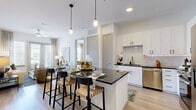 Located in Frisco, TX, this thoughtfully designed single-floor residence offers two bedrooms and two bathrooms within a comfortable and efficiently laid-out floor plan. The living room is bright and welcoming, featuring light hardwood-style flooring, soft sage-toned accent walls, and large glass doors that invite abundant natural light and provide outdoor views. The kitchen is a standout, outfitted with crisp white shaker cabinetry, dark granite countertops, a white subway tile backsplash with under-cabinet lighting, and a full suite of stainless steel appliances including a refrigerator, range, microwave, and dishwasher. The primary bedroom is generously sized with plush carpeting and direct access to its en-suite bathroom, which features a dual-sink vanity with dark granite countertops, white cabinetry, and a tiled soaking tub and shower area. The second bedroom is bright and carpeted, benefiting from natural light through double windows. The second bathroom mirrors the same refined finishes and connects to a walk-in closet with built-in shelving and hanging rods. Both closets provide practical, organized storage solutions throughout the home.