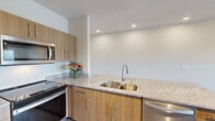 This thoughtfully designed single-floor residence combines contemporary finishes with practical functionality throughout. The kitchen serves as a standout feature, showcasing warm wood-toned cabinetry, light granite countertops with a double stainless steel sink, a glass tile backsplash, and a full suite of stainless steel appliances including a French door refrigerator, electric range, built-in microwave, and dishwasher. Recessed lighting illuminates the workspace effectively.

The living area features smooth light wood-look flooring, track lighting, and large sliding glass doors that open to a private balcony, filling the space with natural light and providing seamless indoor-outdoor access. Additional rooms offer plush carpeting, ceiling fans, and generous windows overlooking lush, open greenery and a scenic landscape, creating a serene and airy atmosphere.

The bathroom is appointed with matching granite countertops, wood-toned cabinetry, tile flooring, and a bright window framing views of the natural surroundings. Bedrooms include ample closet space, adding to the unit's practicality. A dedicated utility room houses a full-size washer and dryer alongside the HVAC system and water heater, offering convenient in-unit laundry. Neutral tones and modern finishes are carried consistently throughout the entire residence.
