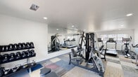 Located at 600 Nottingham Oaks Trail in Houston, TX, this fitness center offers a comprehensive, single-level workout facility designed to accommodate a wide range of exercise needs. The space features a clean, modern aesthetic with crisp white walls, recessed lighting, and a patchwork-style carpet flooring that adds a contemporary touch throughout.

A large floor-to-ceiling mirror spans one wall, visually expanding the space and providing users with proper form feedback during workouts. The cardio section is well-appointed with multiple treadmills and an elliptical machine positioned near large windows that allow natural light to fill the room and offer views of the surrounding exterior.

The strength training area includes a multi-functional cable machine suitable for a variety of resistance exercises, along with a dedicated free weight station stocked with a full rack of dumbbells and kettlebells, as well as a weight bench. A spin bike rounds out the cardio offerings, providing low-impact cycling options.

The facility also includes a small adjacent room or office area, a waste bin, and wall-mounted controls, suggesting attentive facility management. The overall ambiance is bright, functional, and well-maintained, making it a practical and inviting space for daily fitness routines.