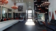 This single-story space makes an immediate impression with its soaring ceiling height, which amplifies the sense of openness throughout the main living area. The design follows a cohesive black, white, and red color scheme that lends the interior a bold, contemporary character. Two ornate red crystal chandeliers serve as dramatic focal points, contrasting with the otherwise clean, minimalist architecture and adding a touch of glamour to the space.

The flooring consists of large-format dark gray tiles that extend across the open layout, grounding the space while complementing the high-contrast décor. A floor-to-ceiling built-in shelving unit in dark tones lines one side of the room, displaying curated decorative objects, books, and accent pieces in coordinating colors. On the opposite side, white upholstered seating with red accent pillows adds comfort without compromising the design aesthetic.

Natural light enters through tall glass entry doors at the far end, casting sunlight across the polished floor and offering a view of the exterior. A striking abstract artwork anchors one wall, reinforcing the bold visual identity of the space. The overall ambiance is modern, curated, and architecturally refined.