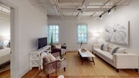 Located at 223 S Holly St in Columbia's vibrant 29205 zip code, this single-floor unit masterfully blends industrial character with modern finishes. Soaring ceilings with exposed steel trusses and painted white brick walls define the aesthetic throughout, while warm hardwood flooring grounds every room with a welcoming tone.

The living area is bright and open, benefiting from multiple windows that invite natural light and views of surrounding greenery. The kitchen is a standout, outfitted with sage-toned shaker cabinetry, white quartz countertops, a subway tile backsplash, stainless steel appliances, and a multi-seat island with pendant lighting above — ideal for both cooking and entertaining.

Multiple bedrooms continue the industrial-chic theme, each featuring the signature exposed truss ceilings, brick accent walls, and generous natural light. The primary bathroom impresses with large-format marble-look tile on both the floors and walls, a glass-enclosed shower, and sleek black hardware accents. A second full bathroom offers a marble-tiled tub and shower combination with the same refined finish palette.

Throughout the space, the interplay of raw architectural elements and polished contemporary updates creates a cohesive, sophisticated atmosphere well-suited to modern urban living.
