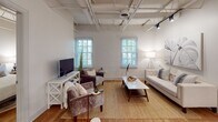 Located at 223 S Holly St in Columbia's vibrant 29205 zip code, this single-floor unit masterfully blends industrial character with modern finishes. Soaring ceilings with exposed steel trusses and painted white brick walls define the aesthetic throughout, while warm hardwood flooring grounds every room with a welcoming tone.

The living area is bright and open, benefiting from multiple windows that invite natural light and views of surrounding greenery. The kitchen is a standout, outfitted with sage-toned shaker cabinetry, white quartz countertops, a subway tile backsplash, stainless steel appliances, and a multi-seat island with pendant lighting above — ideal for both cooking and entertaining.

Multiple bedrooms continue the industrial-chic theme, each featuring the signature exposed truss ceilings, brick accent walls, and generous natural light. The primary bathroom impresses with large-format marble-look tile on both the floors and walls, a glass-enclosed shower, and sleek black hardware accents. A second full bathroom offers a marble-tiled tub and shower combination with the same refined finish palette.

Throughout the space, the interplay of raw architectural elements and polished contemporary updates creates a cohesive, sophisticated atmosphere well-suited to modern urban living.