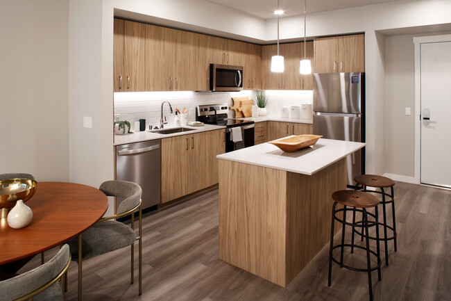 Design Collection II Kitchen with oak cabinetry, white quartz countertops, and white tile backsplash - Avalon Alderwood Place